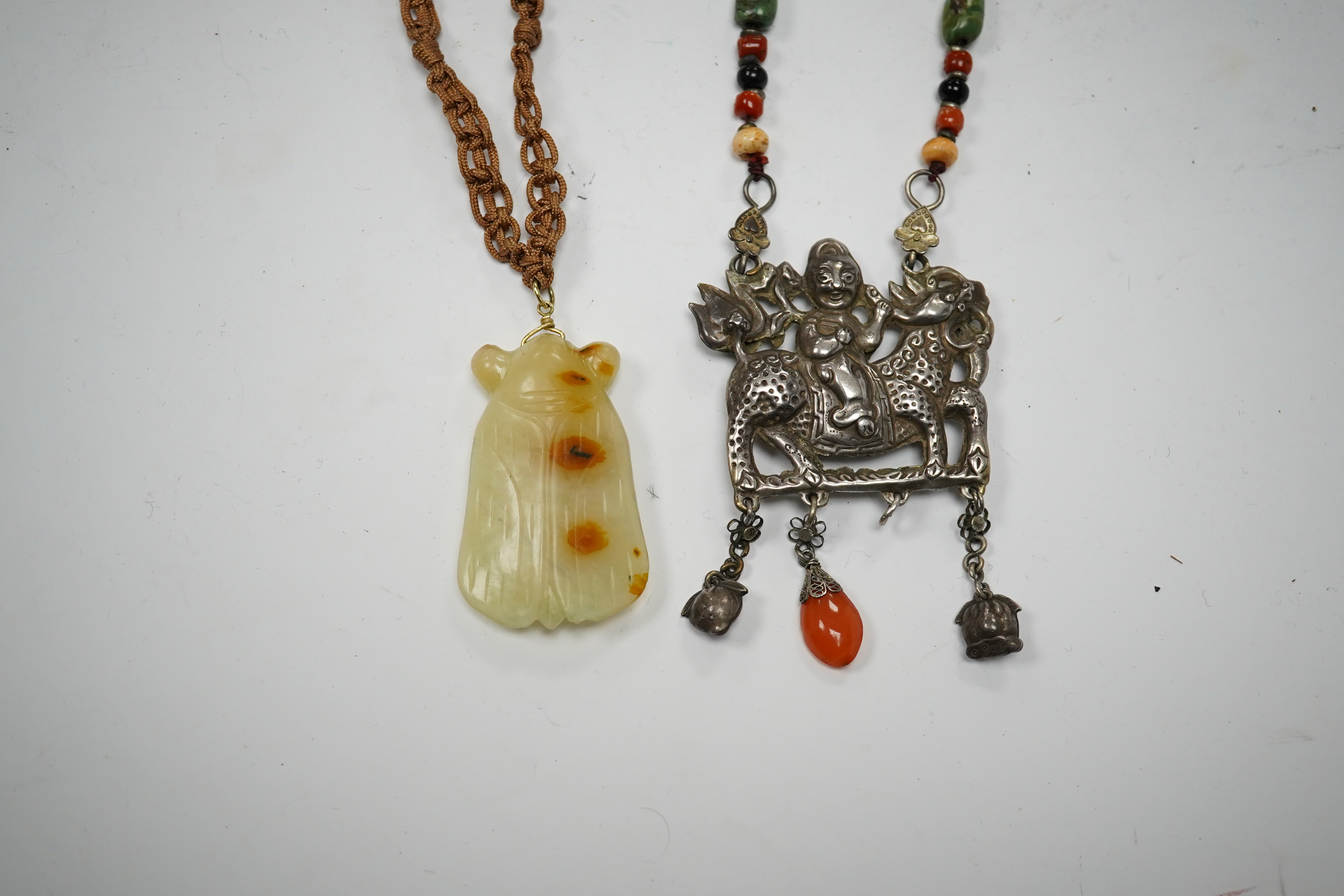 A Chinese celadon and russet jade cicada pendant on cording and a silver and stone mounted chain and pendant of boy riding a qilin, cicada 5.5cm long (2). Condition - tip of cicada wing chipped and on silver pendant one